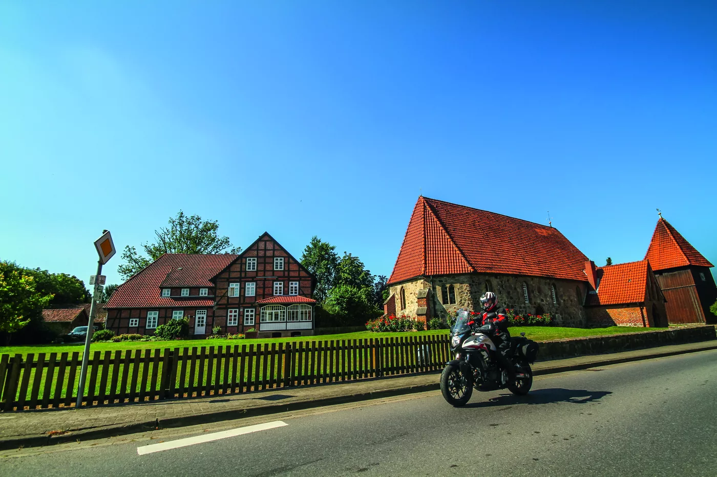 Motorrad auf der Dorfstraße vor Backsteinhäusern und Kirche Motorrad auf der Dorfstraße vor Backsteinhäusern und Kirche
